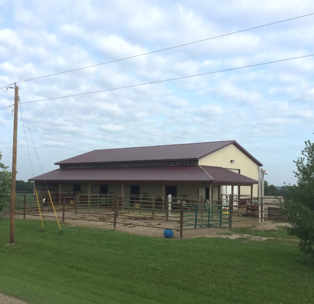 Horse barn with fenced paddock under cloudy sky