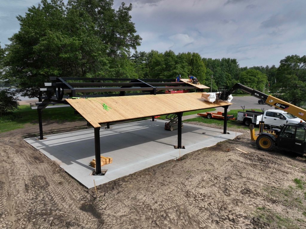 Workers installing wooden roof on steel pavilion frame