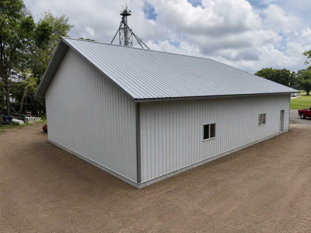 Large white metal barn with gabled roof on gravel lot