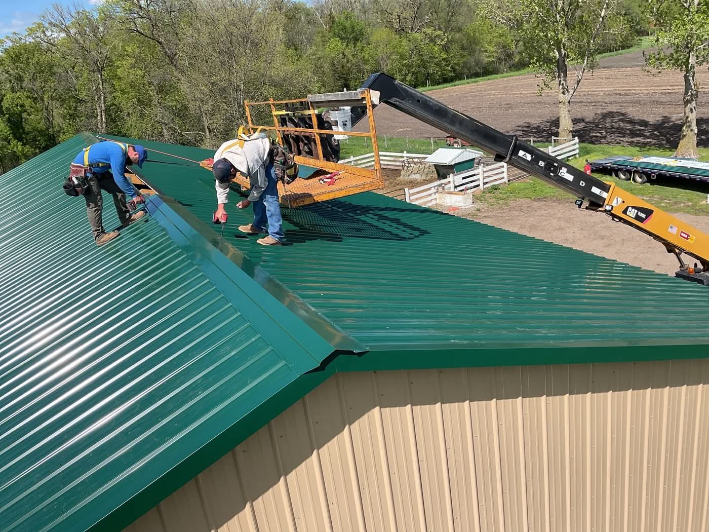 Workers installing green metal roof panels with lift